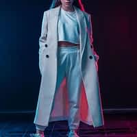 Marina Gold porn actress in white baggy sportswear and white oversized coat posing in room with red and blue lights.