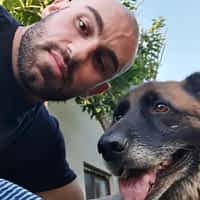 Axel Reed taking a selfie with a German shepherd dog. He is wearing jeans and a black shirt.