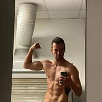 Lando Ryder pornstar posing shirtless in front of a mirror and flexing his biceps. Air vent in the background.
