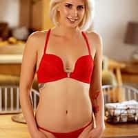 Amy Douxx porn actress in red lingerie posing in front of kitchen table and smiling.