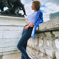 Madison MacQueen porn actress in jeans and white shirt leaning against a concrete railing and looking at a statue.