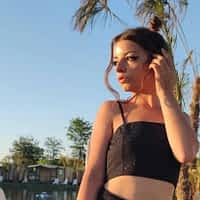 Mary Jane pornstar walking along a pool in black crop top, looking at the sunset.