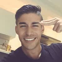 Adrian Dimas porn actor smiling while touching his index and middle finger to his head.