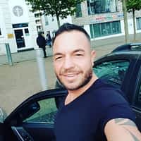 Andy Star pornstar getting out of his car parked at a town square, smiling and wearing a black shirt.