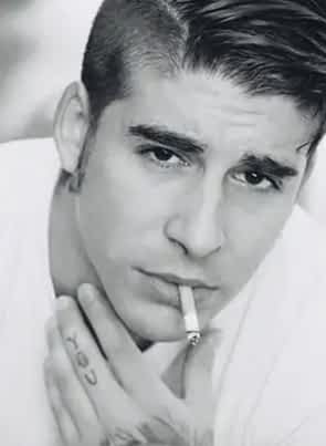 Adrian Dimas smoking a cigarette while rubbing his chin wearing a white shirt in black and white image.