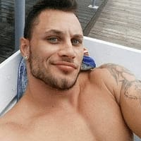 Aris Owner pornstar smiling while taking a selfie, lying on a sun bed with towel behind him.