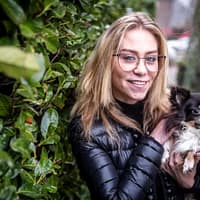 Anouk Maze porn star wearing glasses and holding a dog next to a bush smiling.