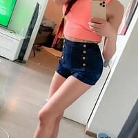 Cindy Sun porn actress posing in front of the mirror of her living room wearing a pink top and jean shorts.