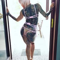 Harleen Van Hynten pornstar standing in front of an openned door in pink see-through underwear, showing her tattooed back.