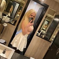 Lisi Kitty pornstar taking a selfie in the bathroom with lots of mirrors around her. Pink crop top and white skirt.