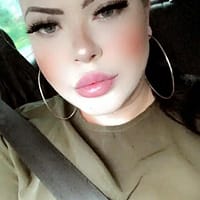 Anastasia XXX porn star in green shirt and her seat belt on, sitting in a car.