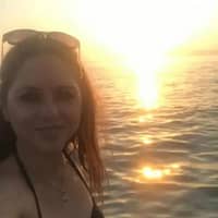 Rachel Adjani porn actress in black bikini top and sun glasses on her head, in front of sunset in the sea.