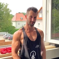 Lando Ryder porn star in oversized workout shirt posing in front of a window showing his muscles.