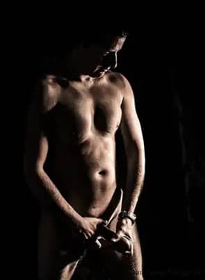 Costas Antonis pornstar standing in a dimly lit room naked and holding his dick.